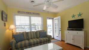 A living room with a sofa, a glass coffee table, a television on a cabinet, and a ceiling fan.