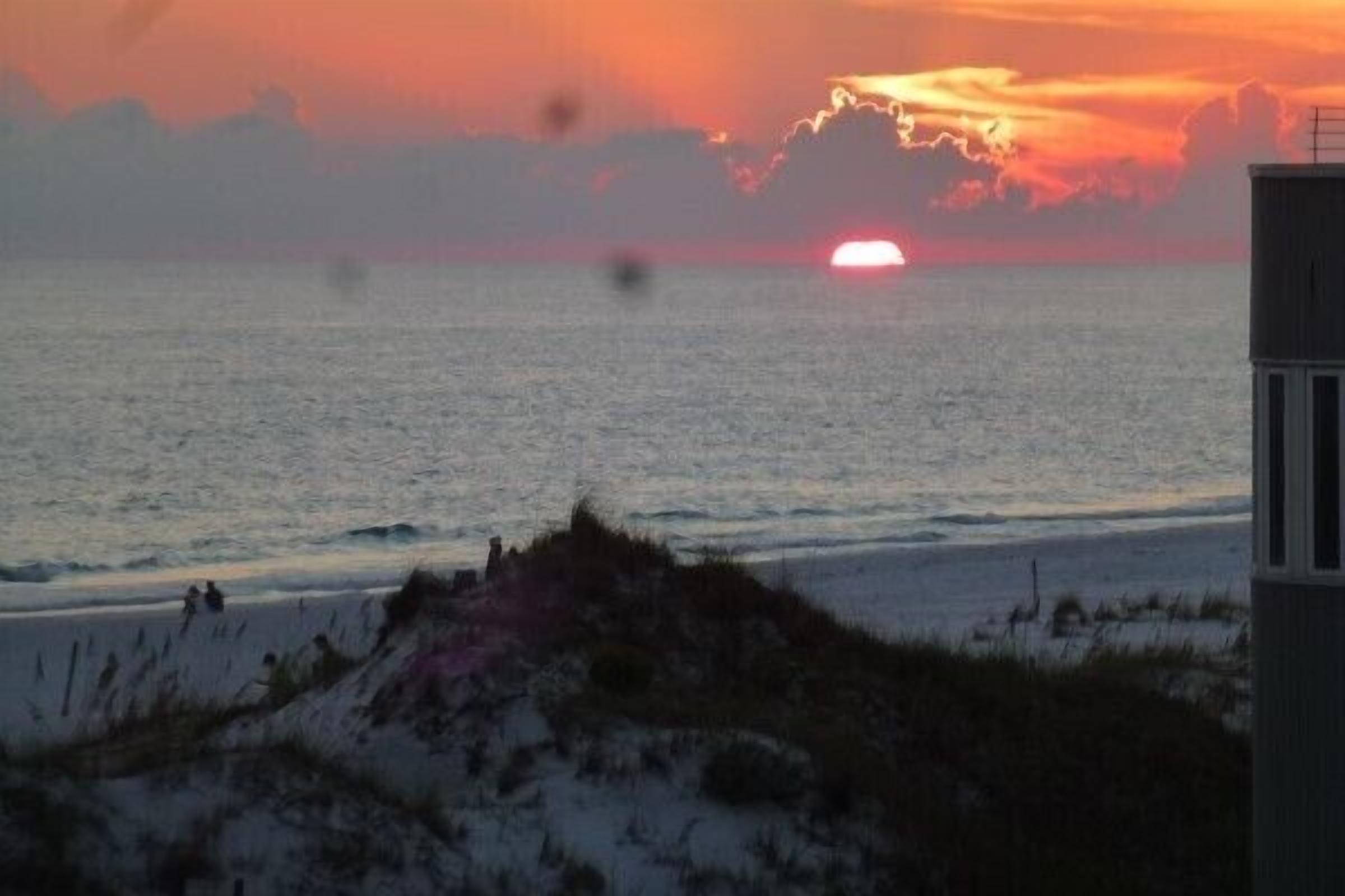 A sunset over a beach with a building in the foreground.