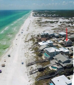 Luchtbeeld van een kustgebied met een strand, huizen en een zwembad.