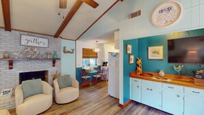 A cozy living room with a fireplace, a dining area with red chairs, and a kitchen with teal walls and wooden cabinets.