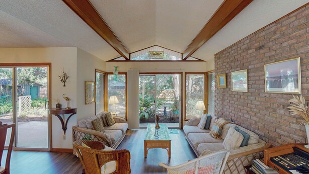 A spacious living room with a high ceiling, large windows, and a brick wall. There are two sofas, a coffee table, and a bookshelf.