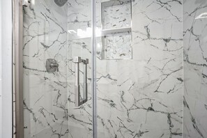 Ein Badezimmer mit Duschkabine aus Glas, Marmorwänden und einem modernen Wasserhahn.
