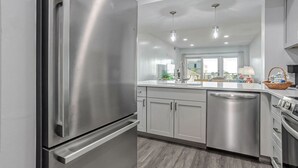 A modern kitchen with stainless steel appliances, a central island with a sink, and a view of the balcony. - Shorewood 332 - Oceanview 3rd Floor Condo (Hilton Head Island)