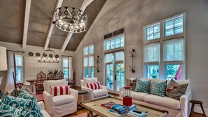 Un salon spacieux avec un plafond haut, de grandes fenêtres et un coin salon confortable agrémenté de canapés blancs et de coussins à motifs.