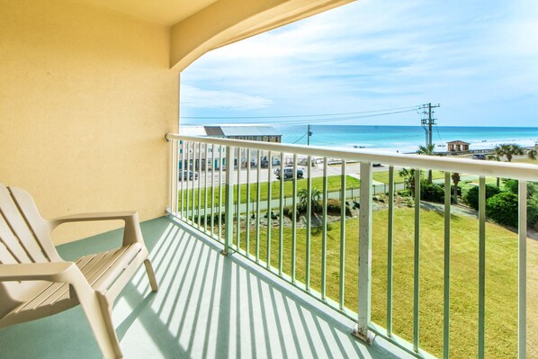 Un balcón con vista a la playa, una silla y un edificio pequeño al fondo.