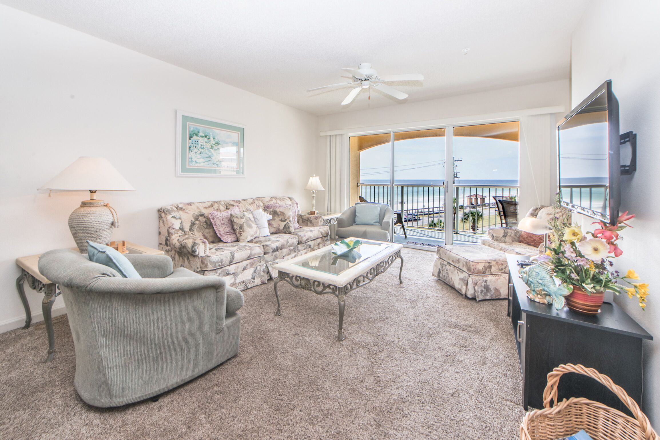 A living room with a sofa, armchair, and coffee table, a television, and a balcony with a view.