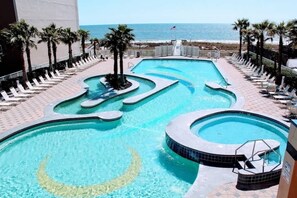 A pool area with multiple swimming sections, palm trees, and a view of the beach.