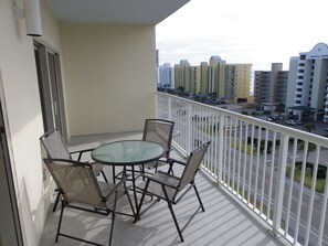 A balcony with a glass table and four chairs, overlooking a street with buildings and parked cars.