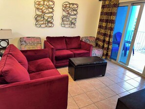 Sala de estar con sofás rojos, un reposapiés negro y sillones estampados. Se observan obras de arte abstracto en las paredes y una vista a través de una puerta de cristal.