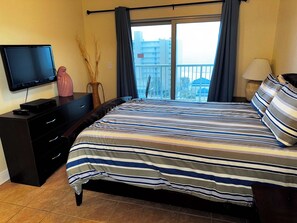 A bedroom with a bed, a TV, a dresser, and a window with curtains.