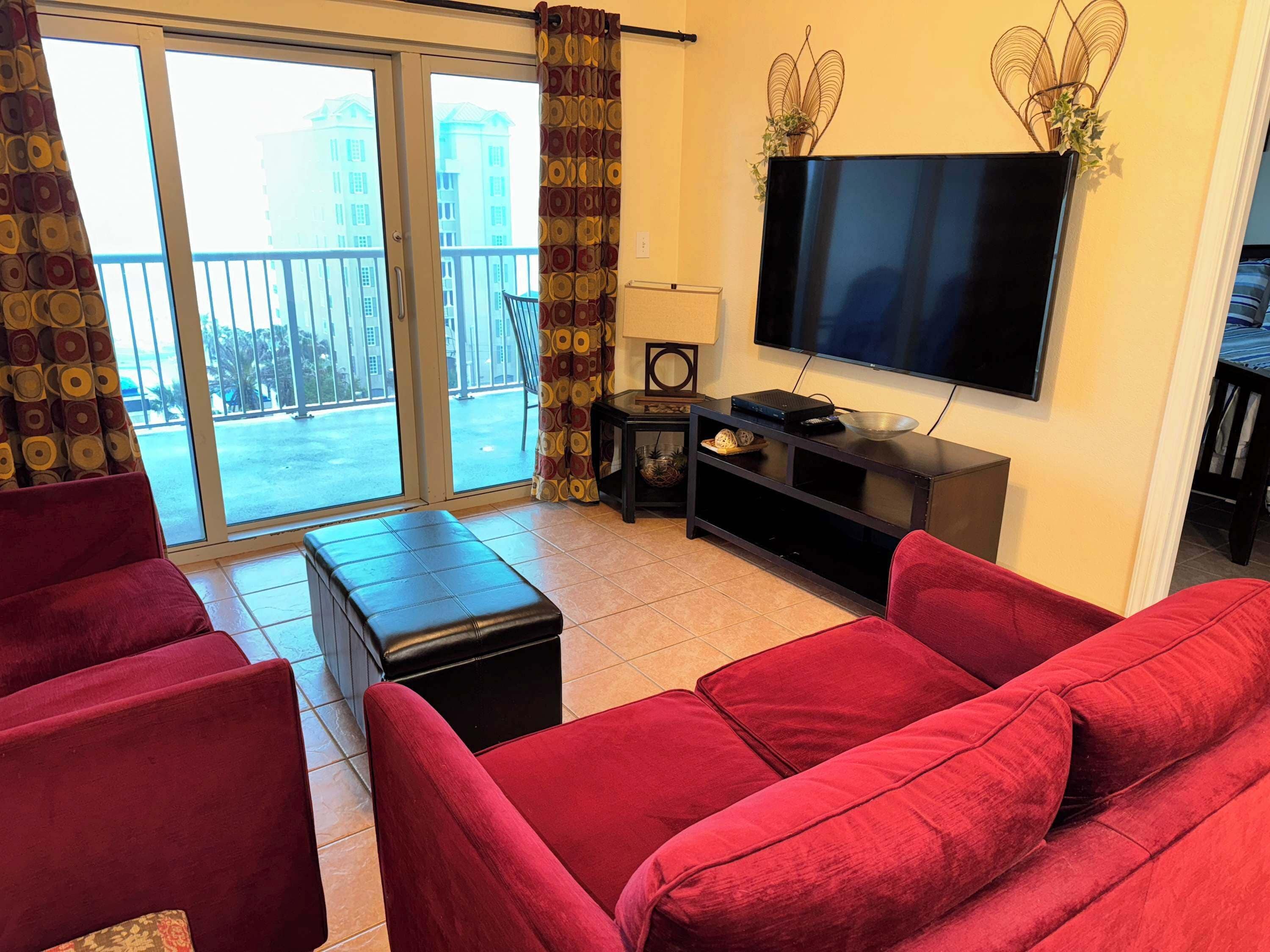 Een woonkamer met rode banken, een flatscreen televisie, een klein zwart tv-meubel en een schuifdeur naar een balkon.