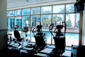 Una palestra con macchinari cardio e ampie finestre con vista su una zona piscina.