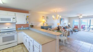 A kitchen with white cabinets, a microwave, and a stove. There is a dining area with a table and chairs.