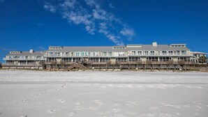 A beachfront hotel with multiple balconies, a sandy beach in the foreground, and a clear blue sky.