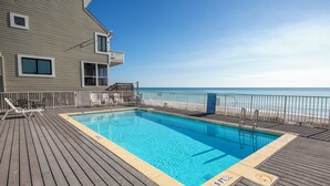 A swimming pool with a wooden deck, lounge chairs, and a view of the beach.