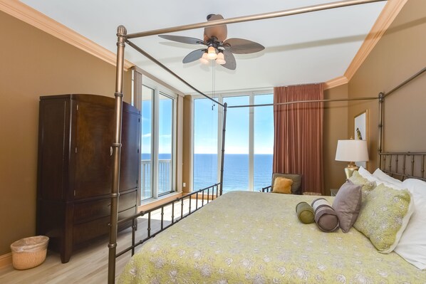 A bedroom with a balcony, a bed with floral bedding, a wooden wardrobe, and a ceiling fan. - Two-story beachfront penthouse w/ extra-large balcony! 🌅 (Destin)