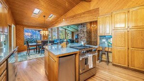 A spacious kitchen with wooden cabinets, a large island with a stove, and a dining area with a view of the outdoors.