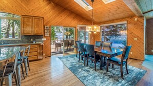 A spacious wooden interior with a dining area, kitchen, and large windows offering views of the outdoors.