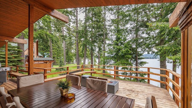 A wooden deck with a table and chairs, overlooking a lake surrounded by trees.