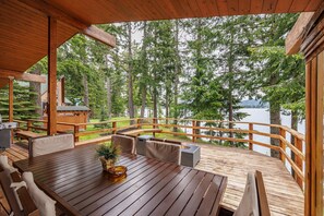 A wooden deck with a table and chairs, overlooking a lake surrounded by trees. - Lakefront Mt Retreat | Peaceful Views, Spa/GameRm + Arrive & Leave at 1PM (Ronald)