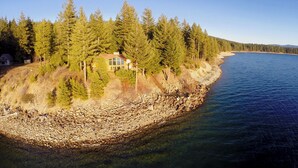 A coastal house surrounded by dense forest, with a clear view of the shoreline and a calm sea.