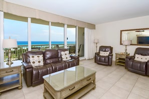 A living room with a leather sofa, armchairs, a glass coffee table, and a view of the ocean.