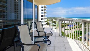 Ein Balkon mit zwei Stühlen und einem Tisch, der Blick auf einen Strand und einen Parkplatz bietet.