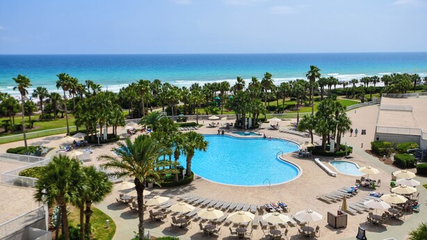 Ein Resort mit einem zentralen Schwimmbad, Palmen und Blick auf den Ozean.