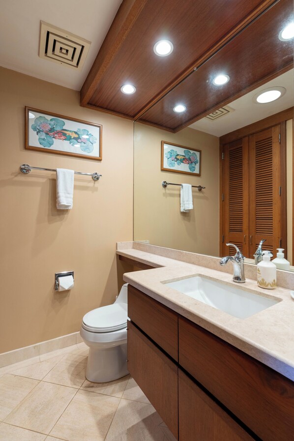 A modern bathroom with a wooden vanity, a white toilet, and a large mirror. - Oceanfront Terrace Condo w/ Private Beach Access! (Kamuela)