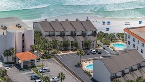 Un hôtel situé en bord de mer, composé de plusieurs bâtiments à étages, doté d’une piscine et de parasols de plage.
