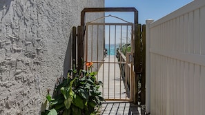 Une entrée fermée par un portail mène à une terrasse en bois offrant une vue sur la mer.
