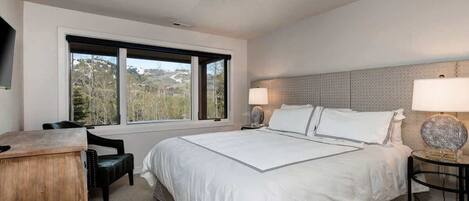 Un dormitorio con una cama grande, un escritorio, una silla, una lámpara y vistas al exterior.