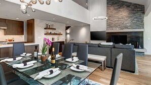 Uma sala de jantar moderna com mesa de vidro, lustre de metal e lareira de pedra.