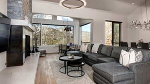 Uma sala de estar moderna com lareira, janelas amplas, sofá modular e área de jantar.
