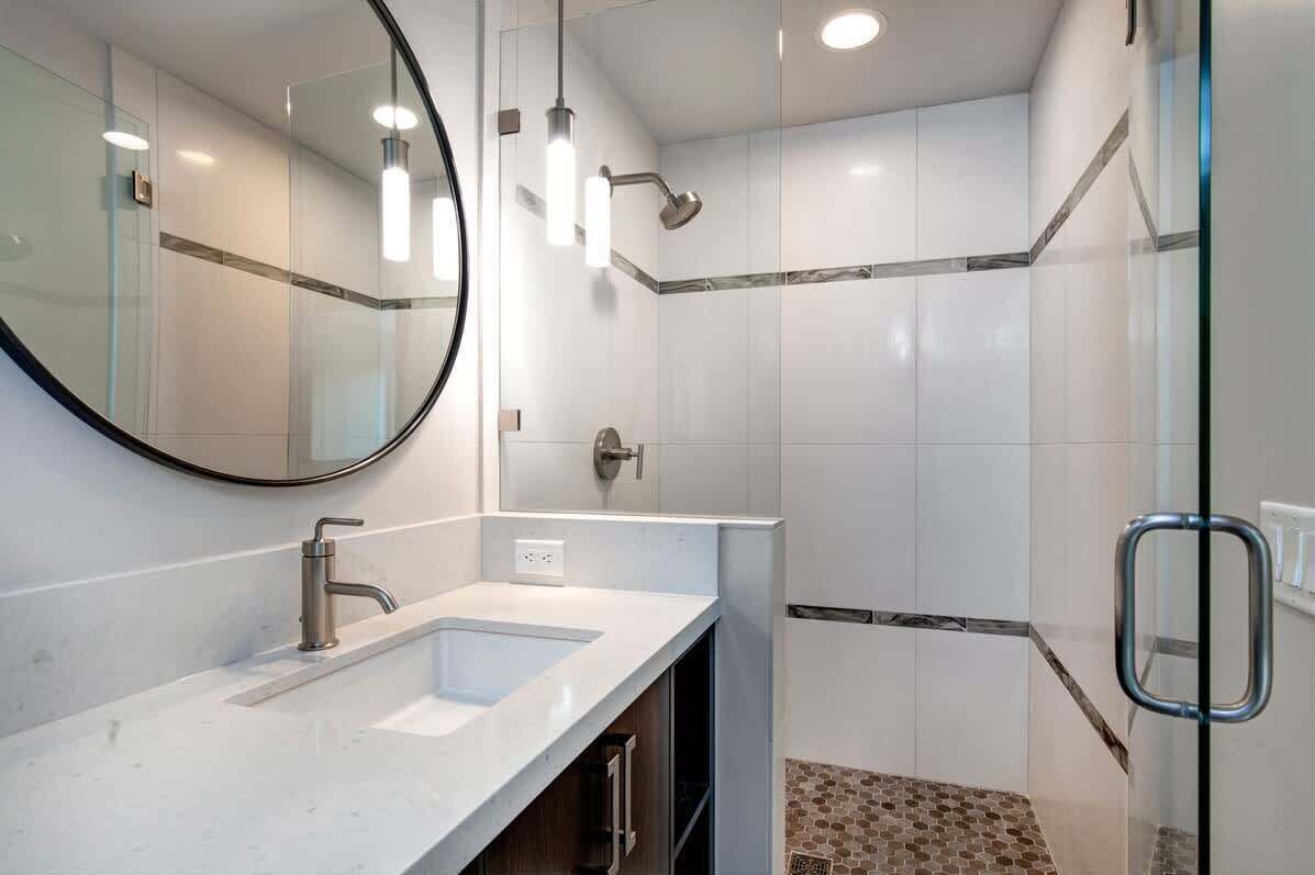 A modern bathroom with a large mirror, two sinks, a shower, and a glass-enclosed shower area.