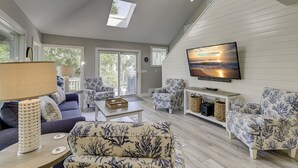 Ein geräumiges Wohnzimmer mit großem Fernseher, gemusterten Möbeln und Blick ins Freie.