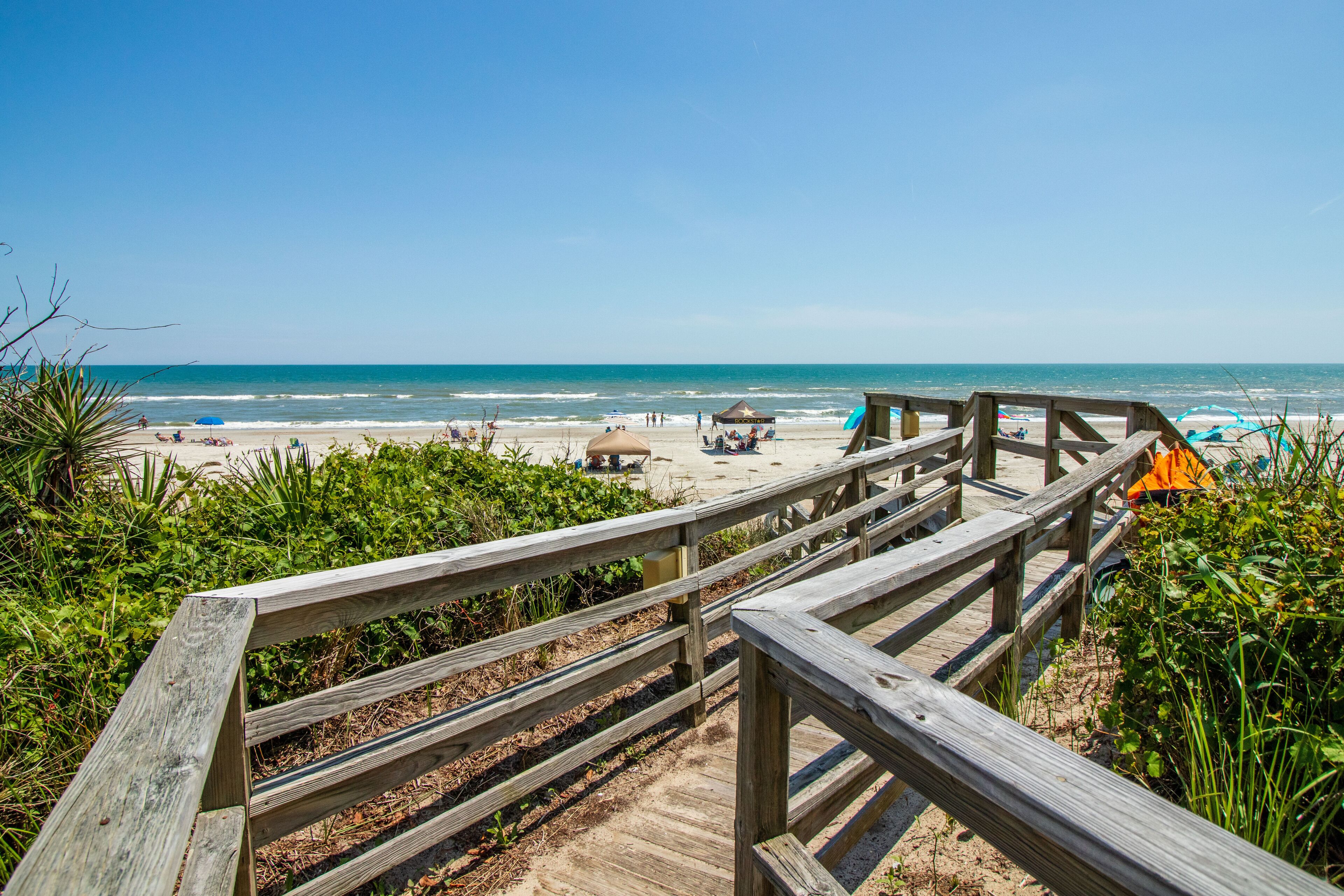 A wooden boardwalk leading to a beach with umbrellas and beach chairs.
