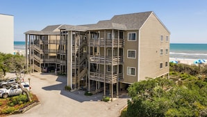 A multi-story building with a central staircase and balconies, located near a beach with umbrellas. - 3 NIGHT MINIMUM SUMMER SPECIAL!!! GREAT FOR GUEST WHO CAN'T STAY A WEEK!!! (Pine Knoll Shores)