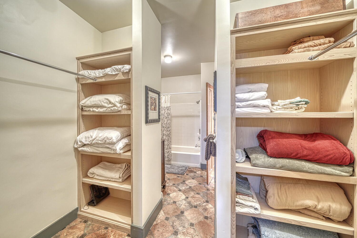 A walk-in closet with multiple shelves for folded clothes and a visible door leading to a bathroom with a bathtub.