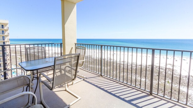 A balcony with a glass table and chairs overlooking a beach.