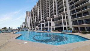 A modern high-rise building with a swimming pool and sun loungers.