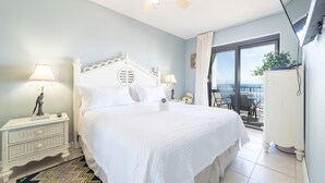 A bedroom with a bed, nightstands, a ceiling fan, and a balcony with a view.