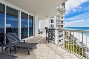 Un balcon avec vue sur la plage, une table et deux chaises longues.
