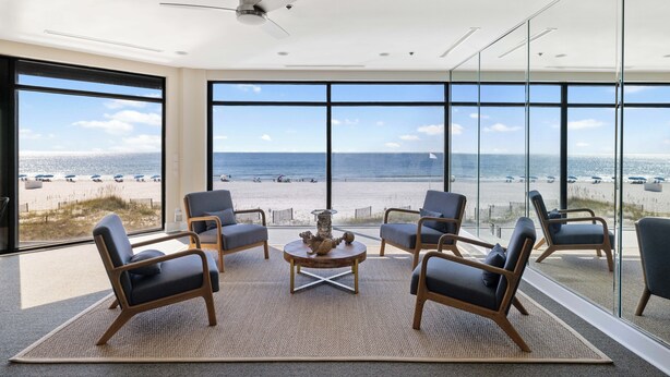A modern room with a large window overlooking a beach, furnished with chairs and a coffee table. - Broadmoor 901 by Liquid Life (Orange Beach)
