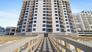 A multi-story residential building with balconies, a wooden boardwalk leading to the entrance, and a clear sky. - Broadmoor 901 by Liquid Life (Orange Beach)
