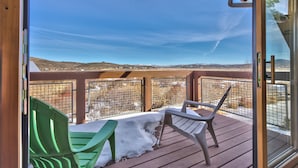Um terraço com duas cadeiras e uma mesa, com vista para uma paisagem nevada e colinas ao longe.