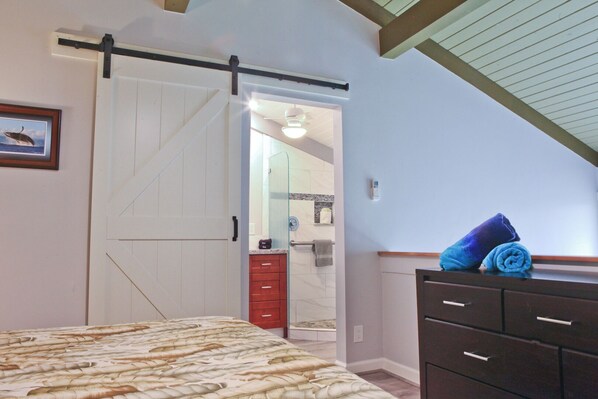 Un dormitorio con cama, un armario, una puerta corredera y un baño visible a través de la puerta.