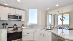A modern kitchen with white cabinetry, stainless steel appliances, and a large window providing natural light. - 4 BR Gulf-Front Condo | Silver Beach Towers E 1101 | Sleeps 10| Book Now! (Destin)