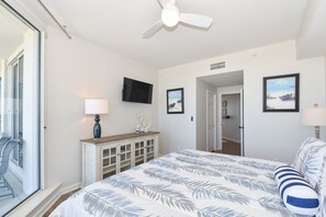 Un dormitorio con cama, ventilador de techo, televisor y ventana.