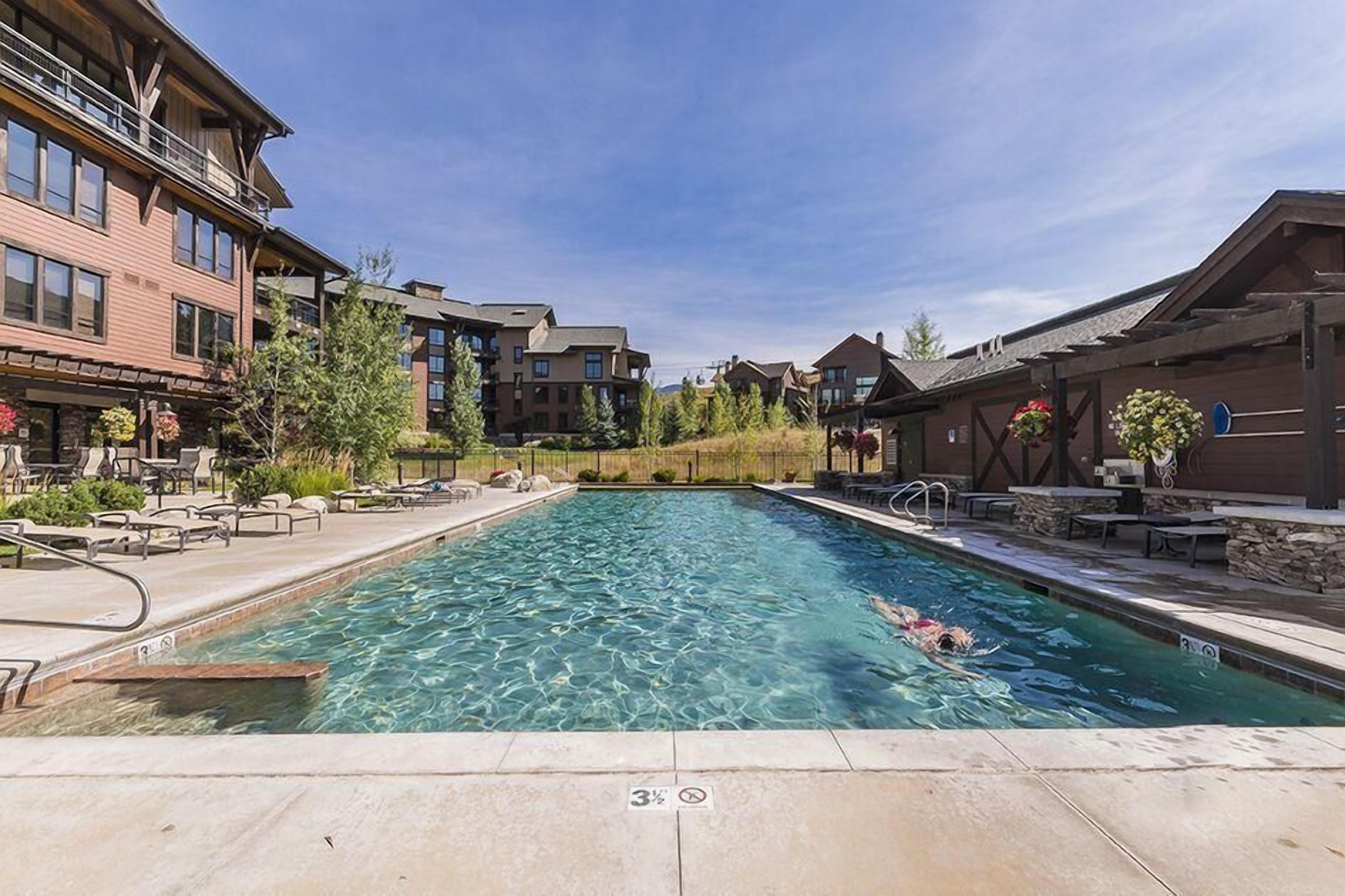 A swimming pool with clear water, surrounded by lounge chairs and a building with multiple floors.